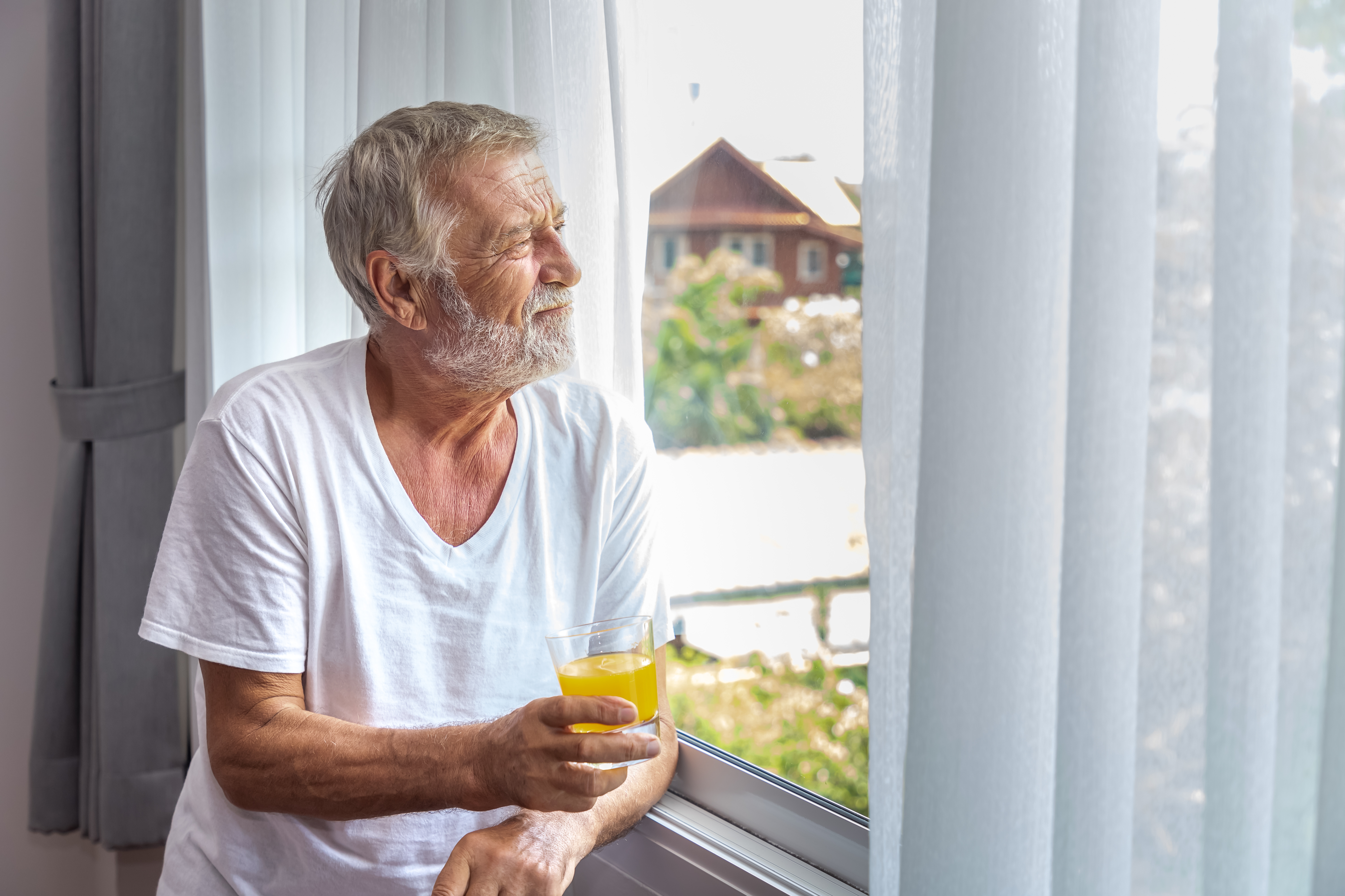 older man looking out window holding glass of juice