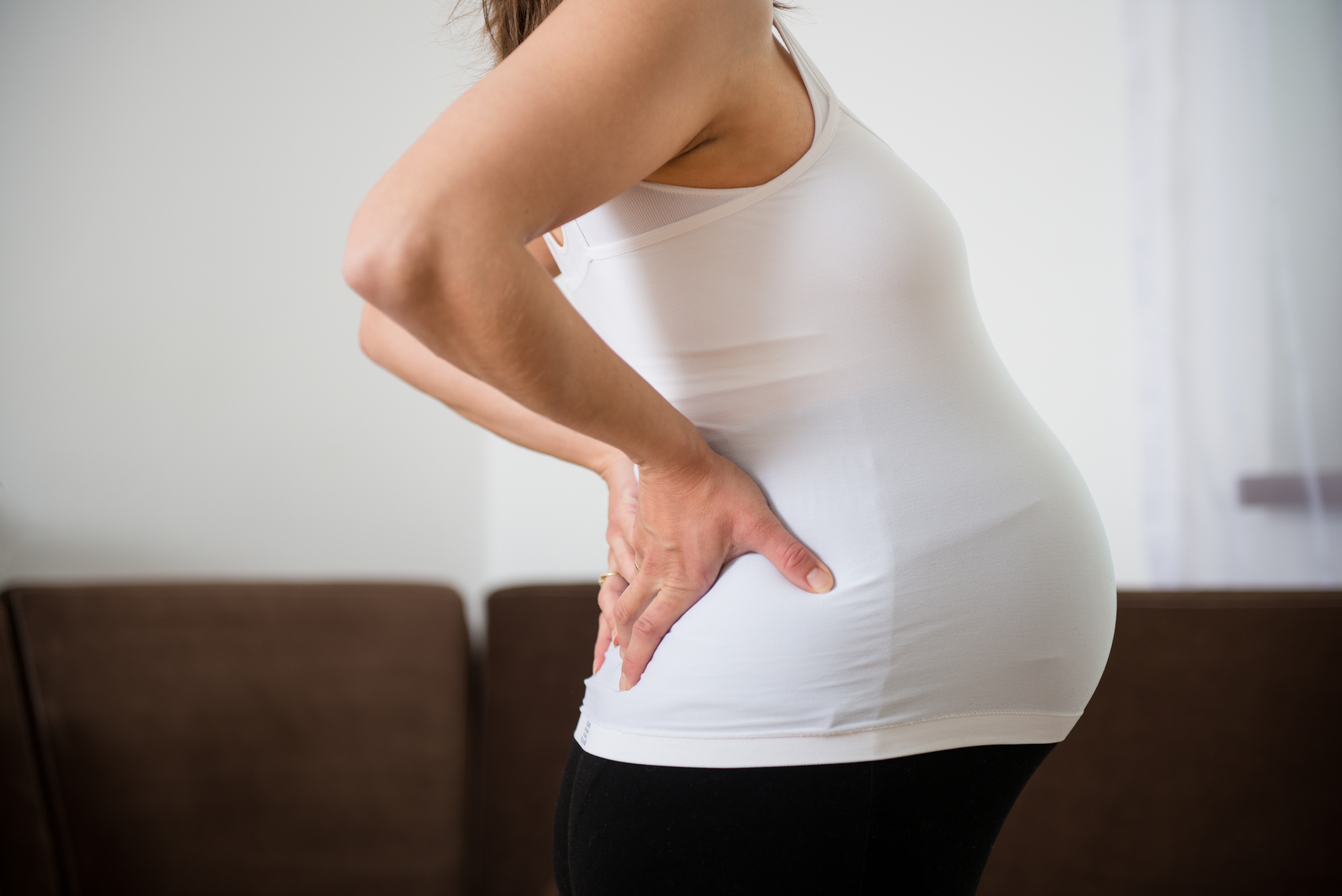 Pregnant person standing in profile with hands on lower back