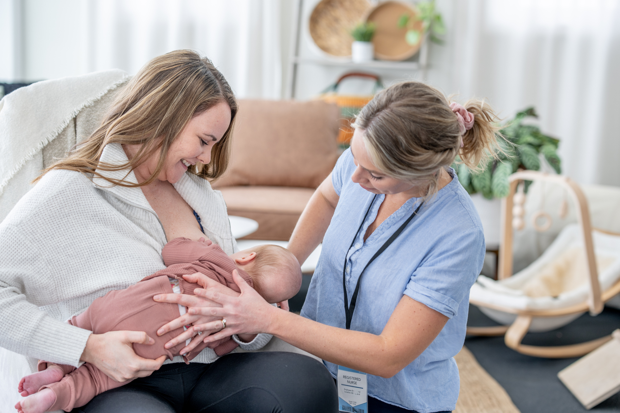 nurse helping mom breast feed her baby while sitting on a couch