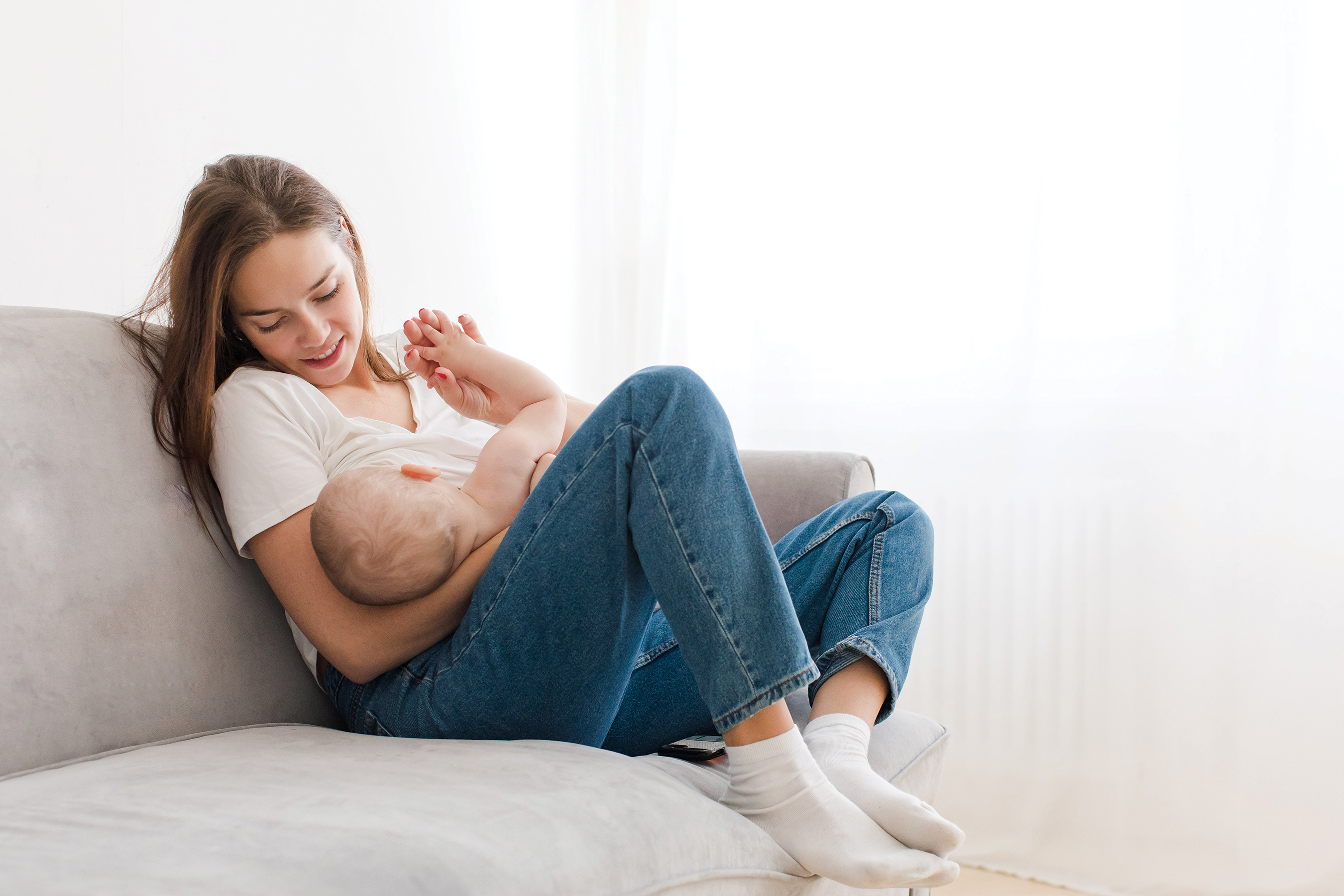 Mother sits on couch nursing her baby.