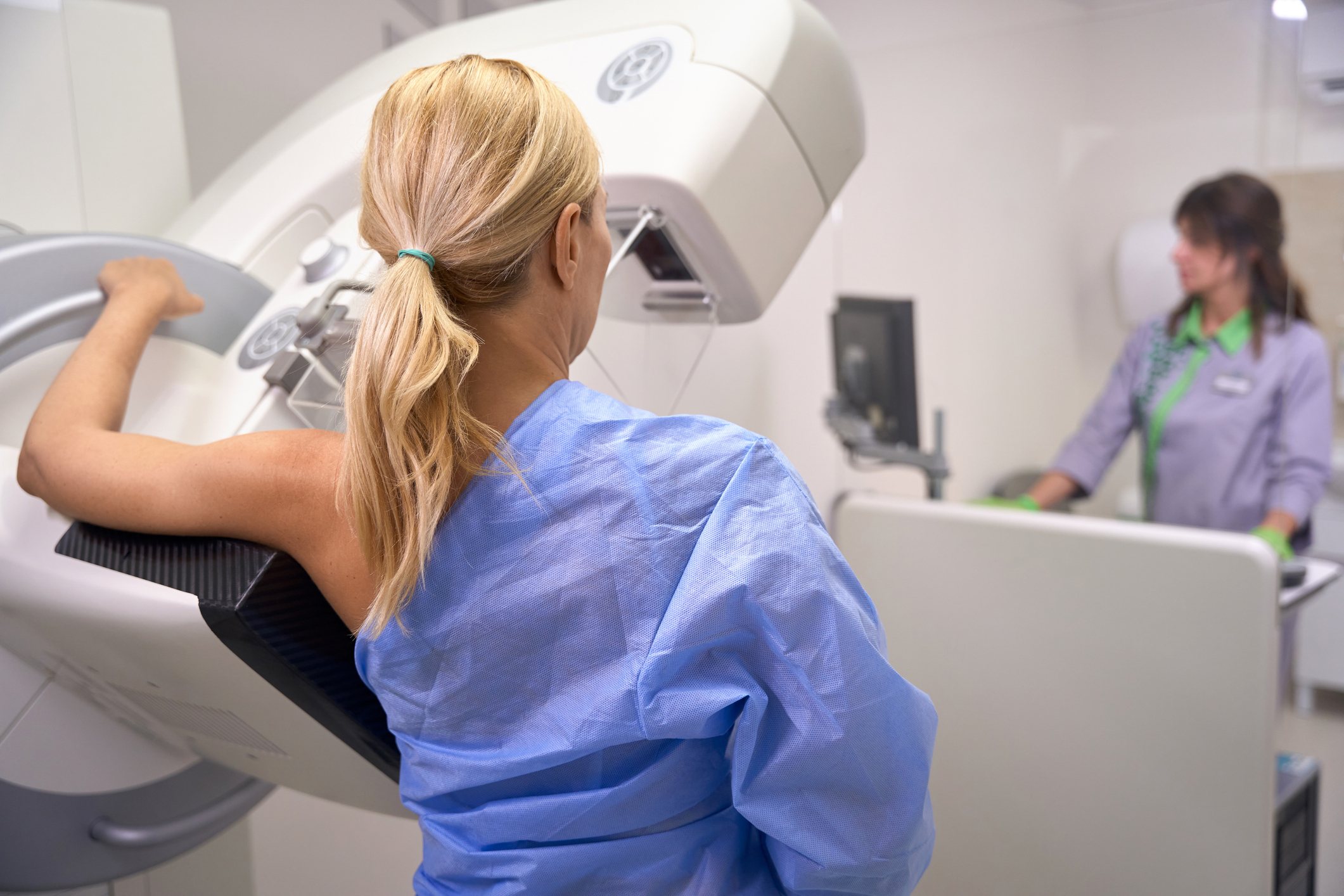 A woman stands next to mammography x-ray machine as technologist takes images.