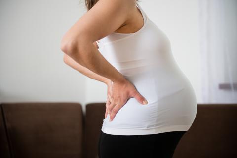 Pregnant person standing in profile with hands on lower back
