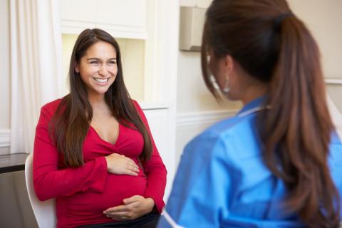 Smiling pregnant person sits talking with provider
